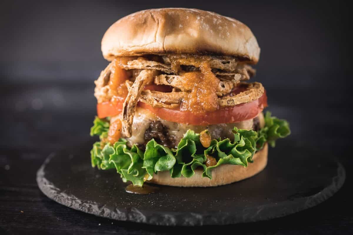 Burger with lettuce, tomato, sauce, and onion straws.