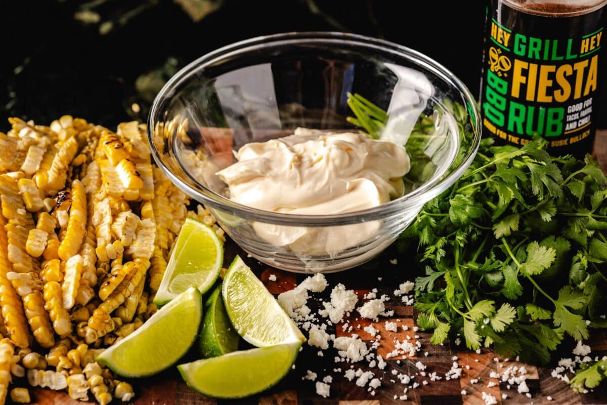 Glass bowl with mayo, surrounded by lime wedges and other ingredients for dressing.