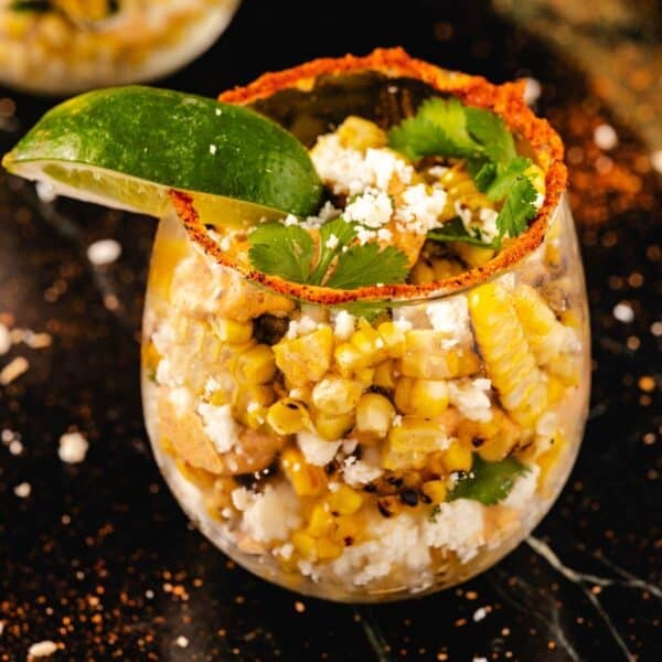 Stemless wine glass filled with corn salad, garnished with seasoned rim and lime wedge.