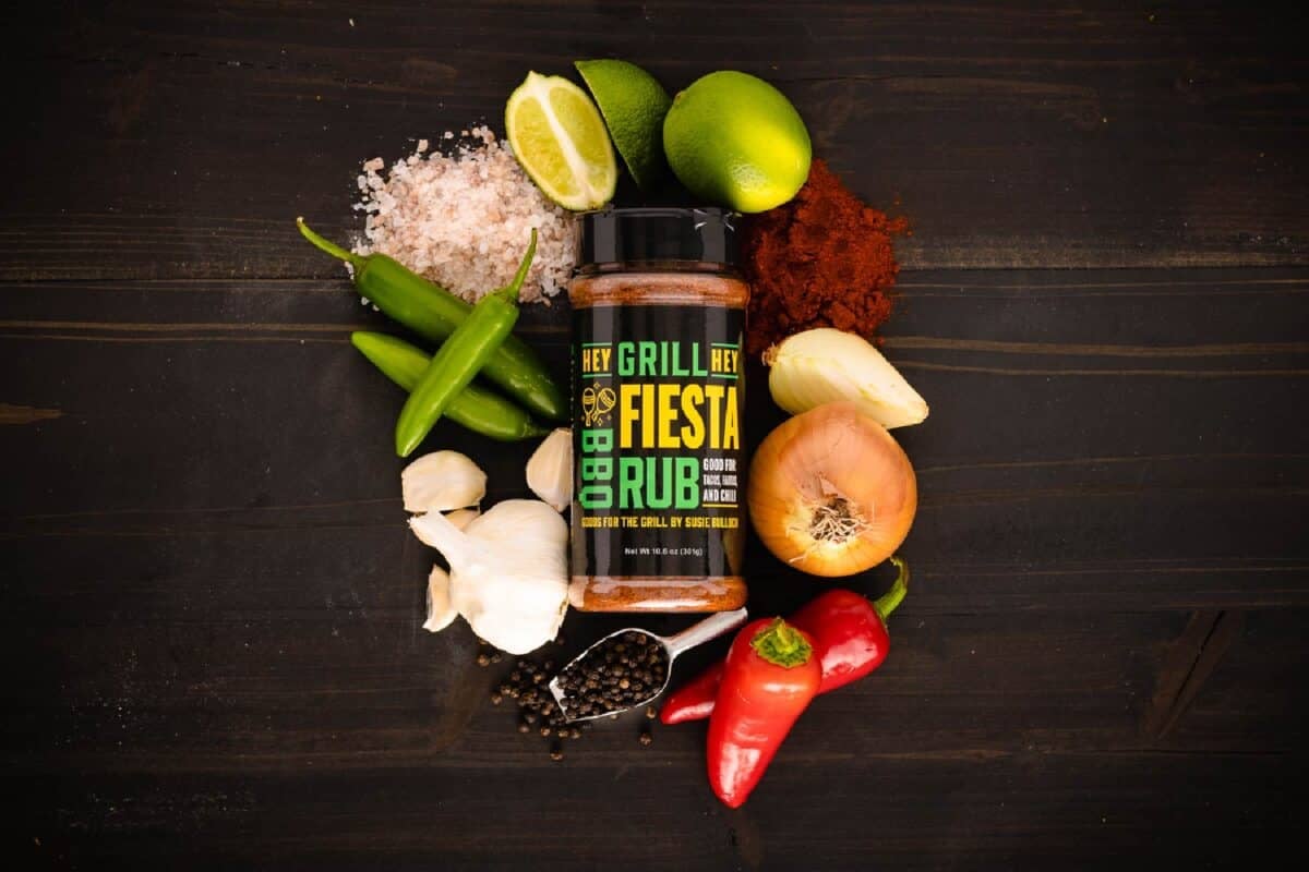 Bottle of seasoning surrounded by raw ingredients on a black countertop.