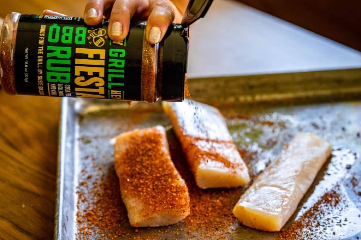 Fish fillets on baking sheet being sprinkled with seasoning.