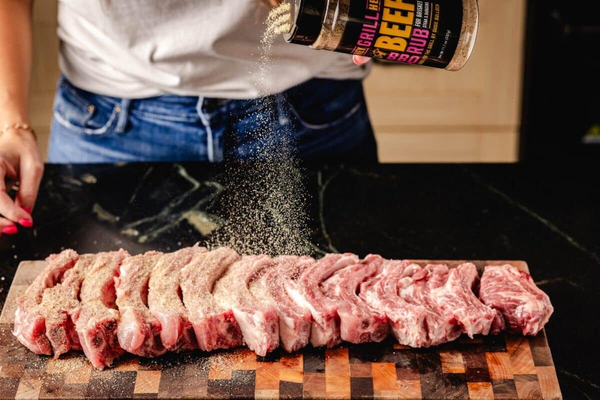 Sliced ribs on cutting board being seasoned with Beef Rub.