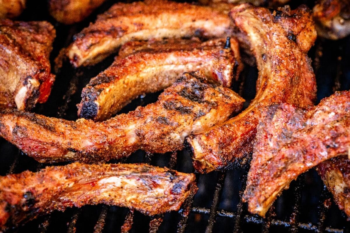 Grilled baby back ribs on grill grates over flames.