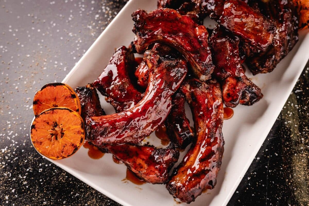 Glazed ribs on white plate with grilled, halved oranges.