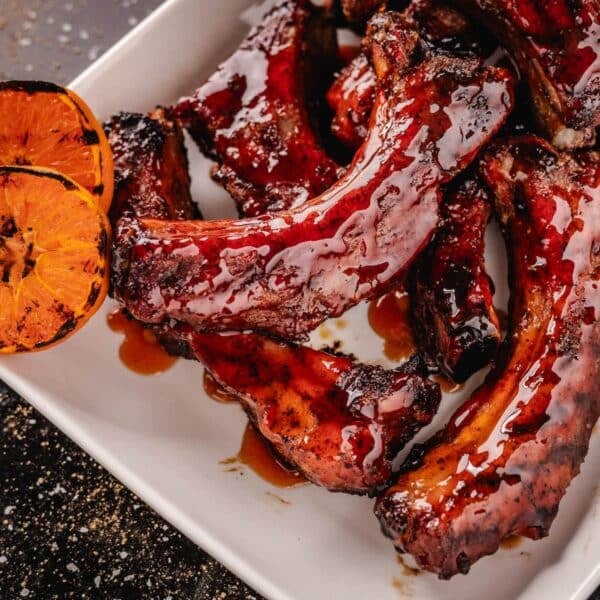 Sliced, glazed party ribs on white place with grilled orange slices.