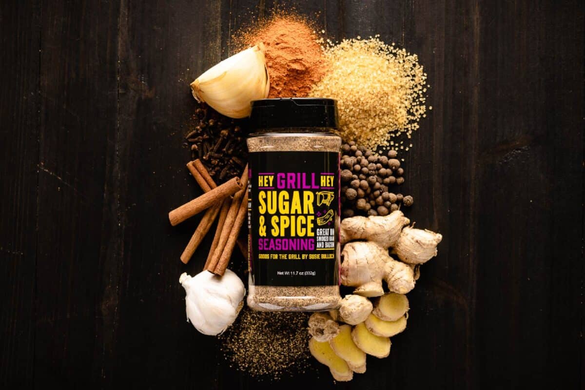 Jar of Sugar & Spice Rub surrounded by raw ingredients on black tabletop.