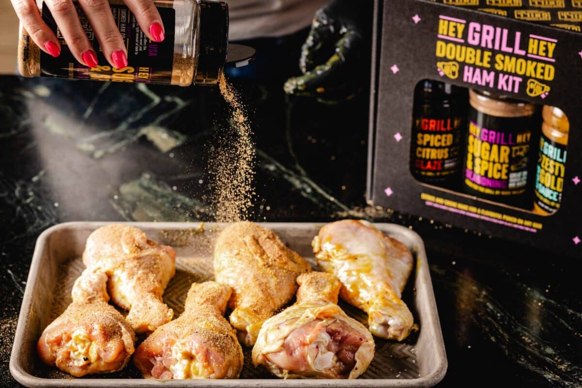 Chicken on a baking sheet being sprinkled with rub, in front of the Double Smoked Ham Kit.