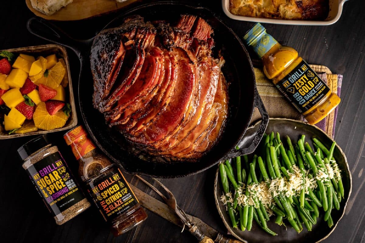 Smoked spiral ham next to green beans and bottles of sauces and rub.