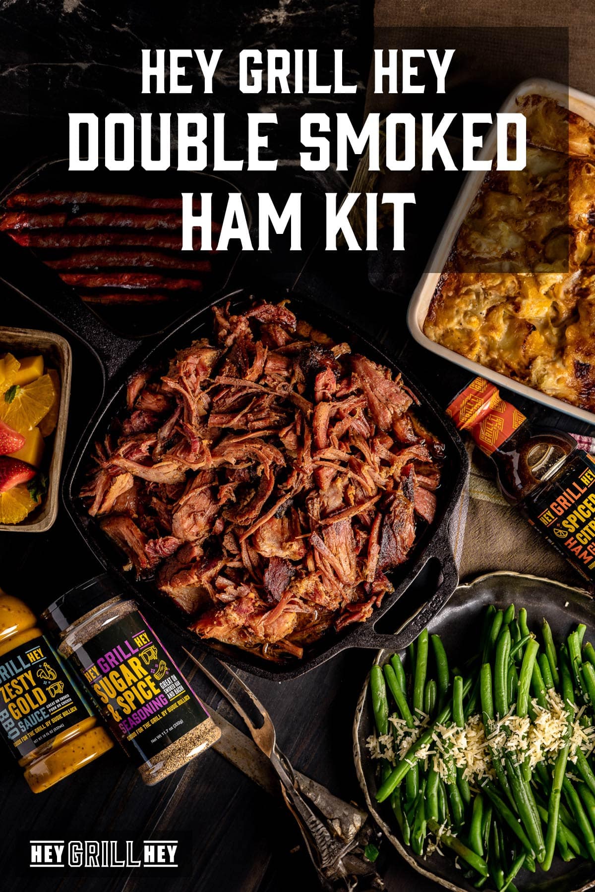 Pulled ham next to sides, and bottles of rub, glaze, and sauce. Text reads "Hey Grill Hey Double Smoked Ham Kit."