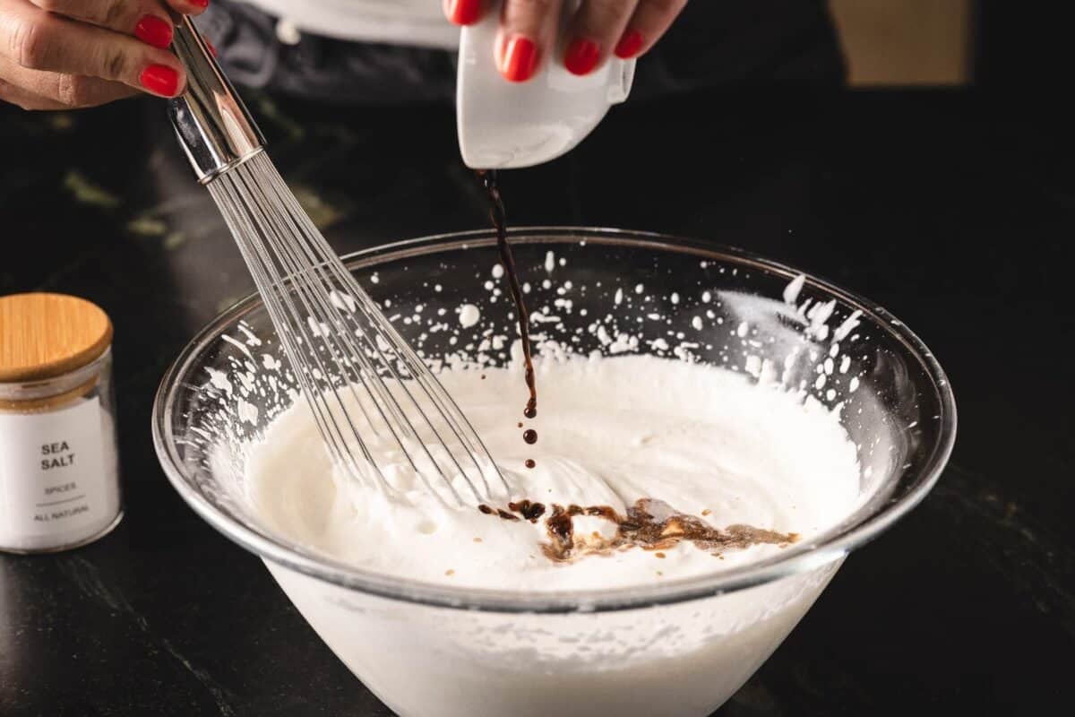 Vanilla extract being poured into glass bowl of cream being whisked.