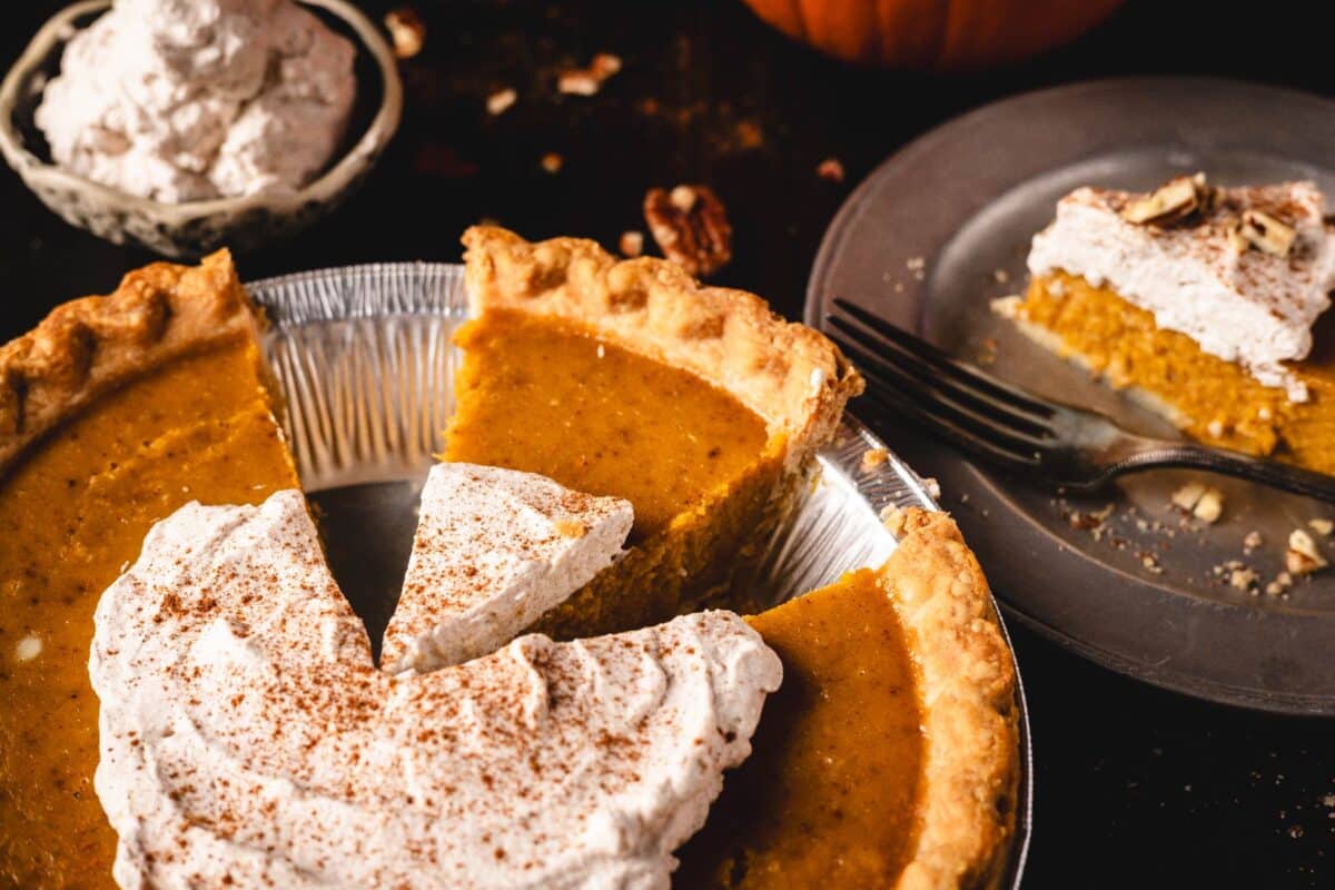 Pumpkin pie in tin with a slice cut out.