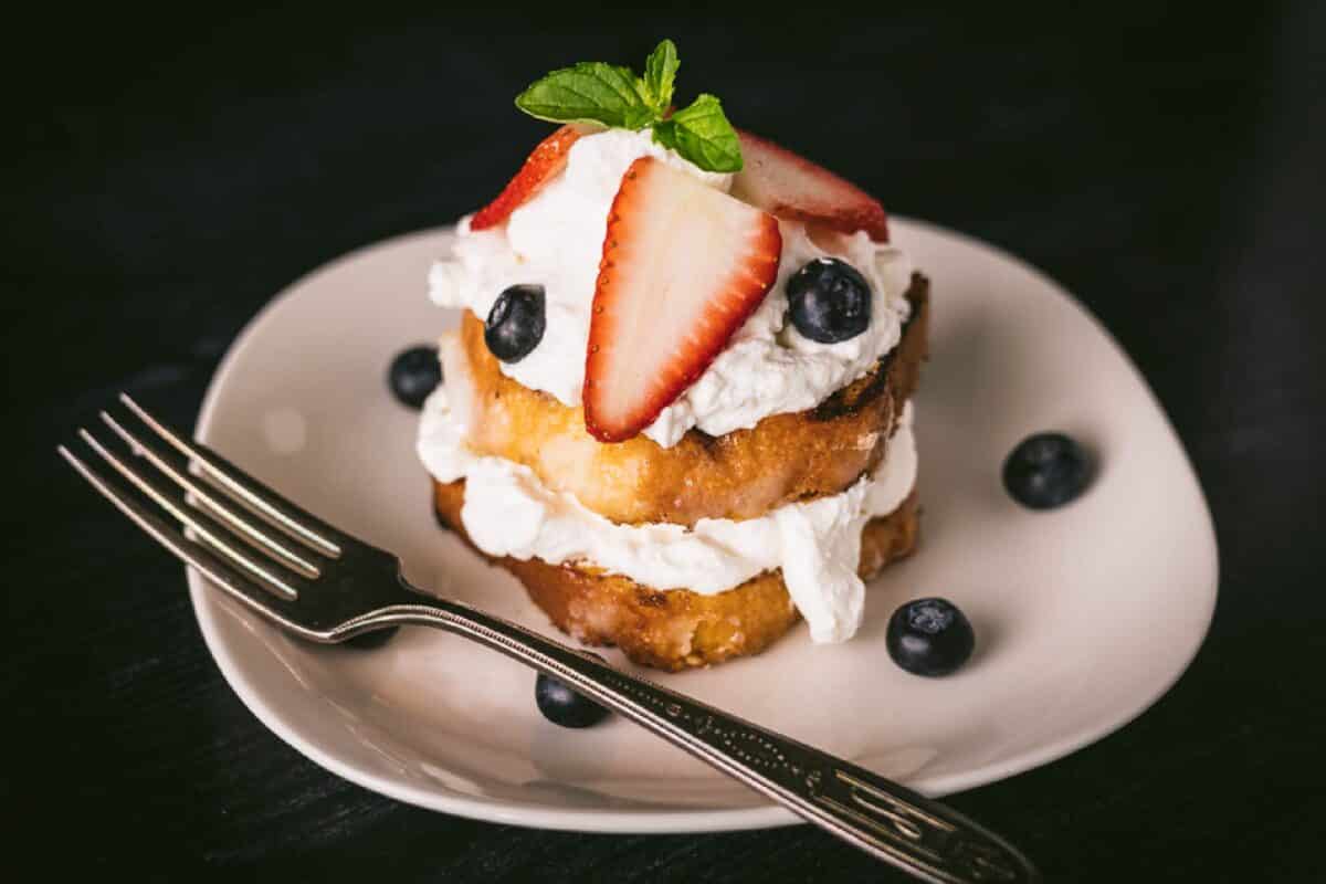 Lemon cake topped with fresh berries and whipped cream on plate with fork.