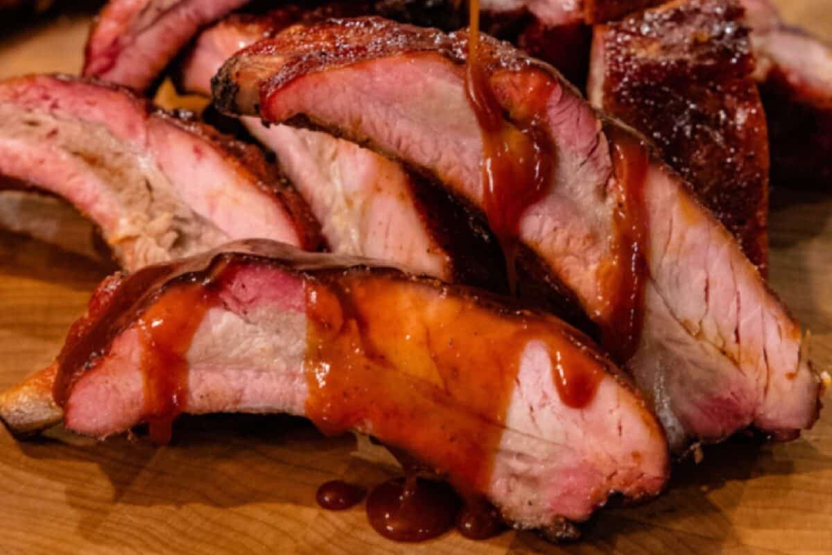 Sliced ribs drizzled with sauce on wooden platter.