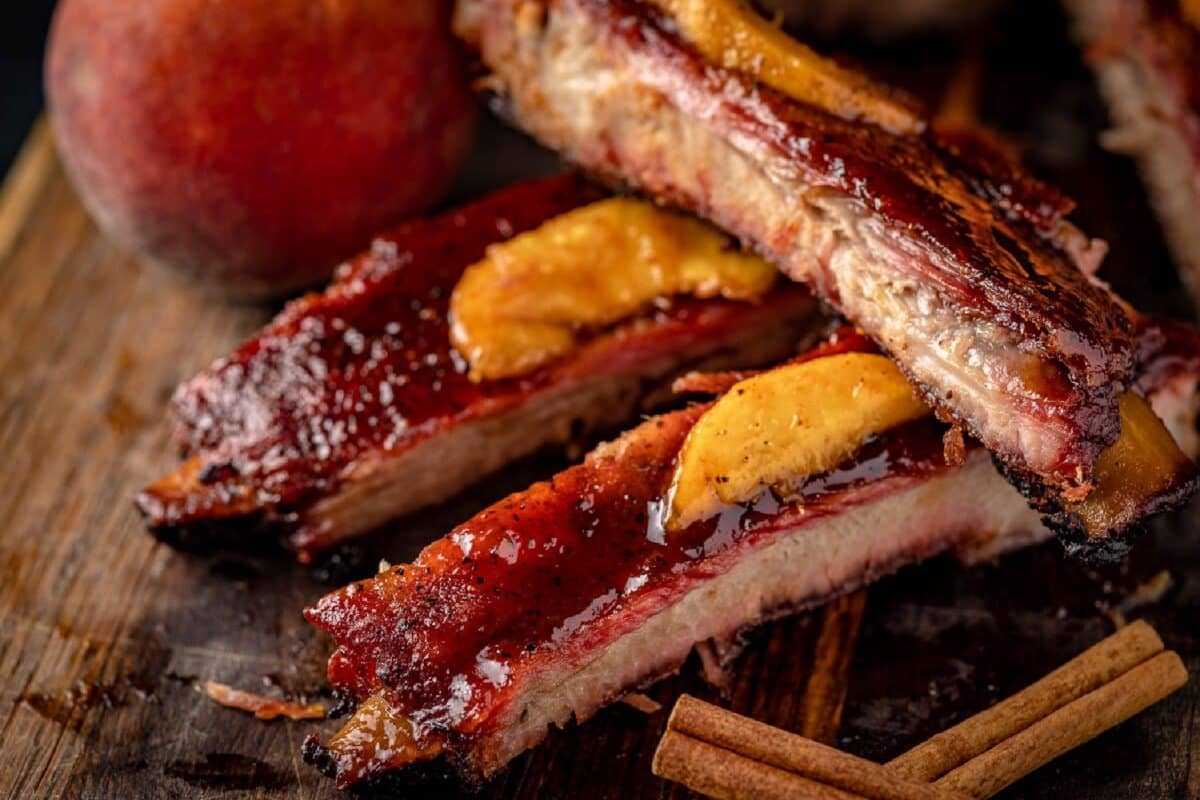 Sliced ribs topped with peach slices, next to cinnamon sticks.