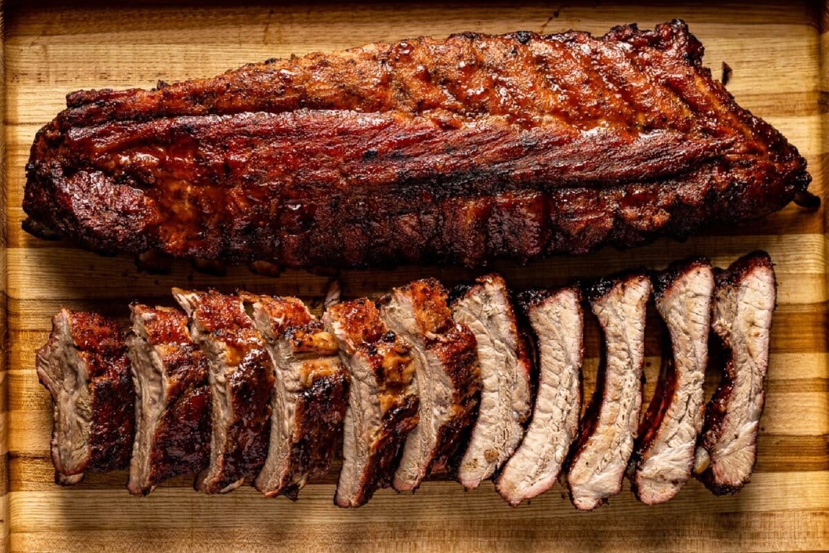 Full rack and sliced rack of ribs from the grill on a wooden cutting board.