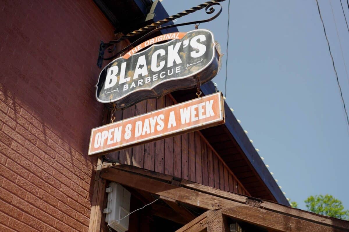 A sign hanging out from the side of a building that reads "Black's Barbecue Open 8 Days a Week".