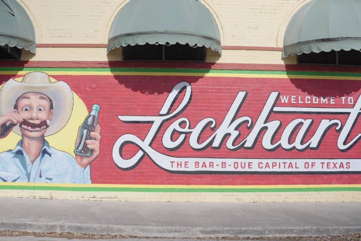 A brick wall with a painted mural of a cowboy that reads "Welcome to Lockhart the Barb-B-Que Capital of Texas".