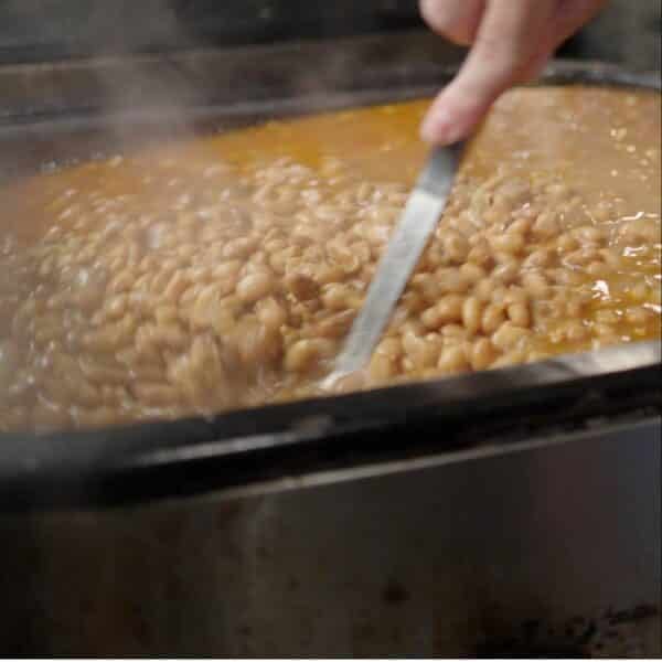 Pinto beans in large pot being stirred with metal spoon.