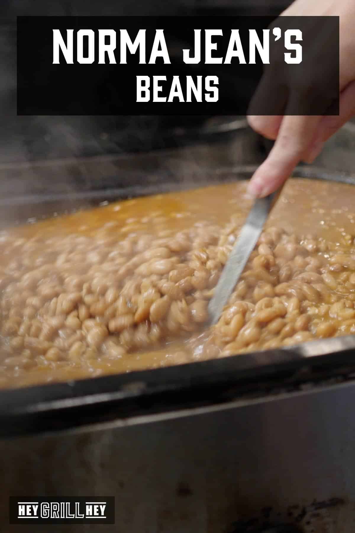 Beans in pot being stirred with metal spoon. Text reads "Norma Jean's Beans".