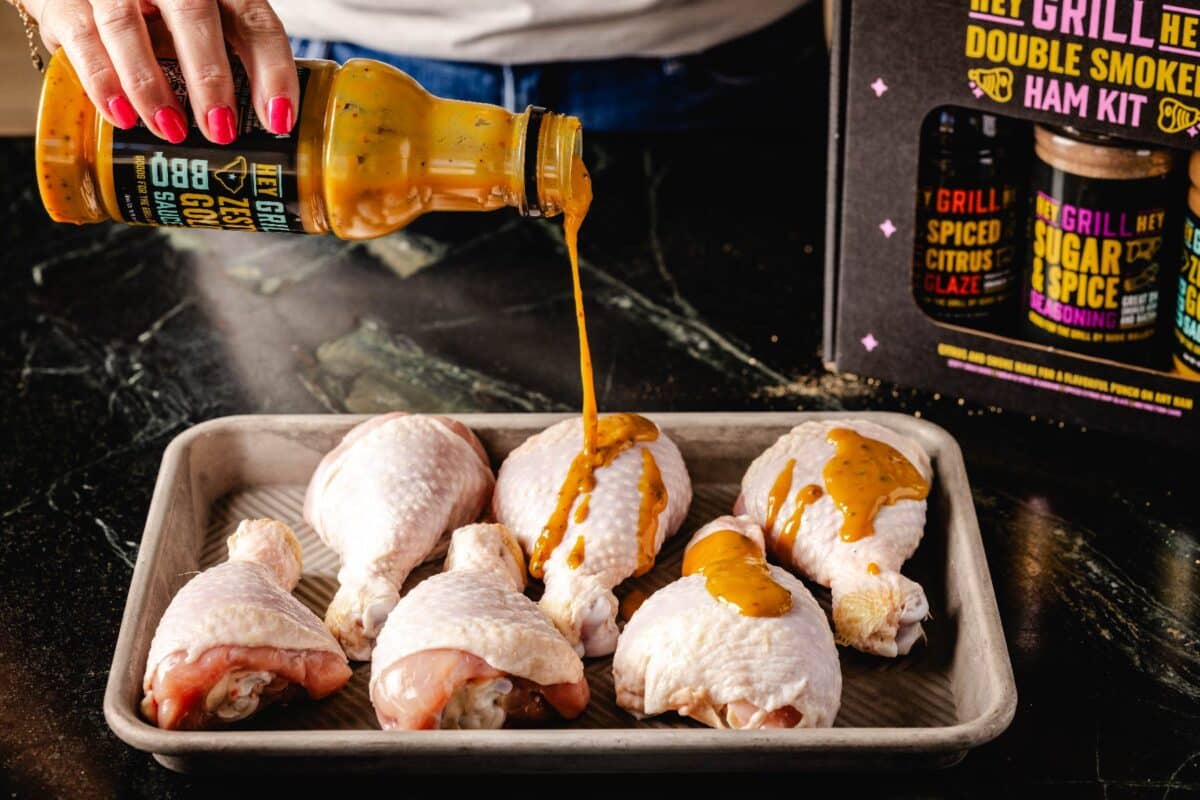 Chicken legs on baking sheet being drizzled with Zesty Gold Sauce.