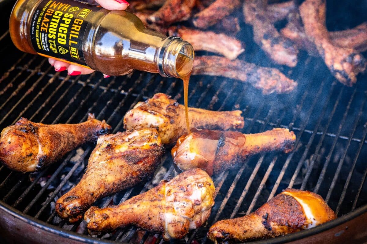 Chicken legs on the grill being drizzled with Spiced Citrus Glaze.