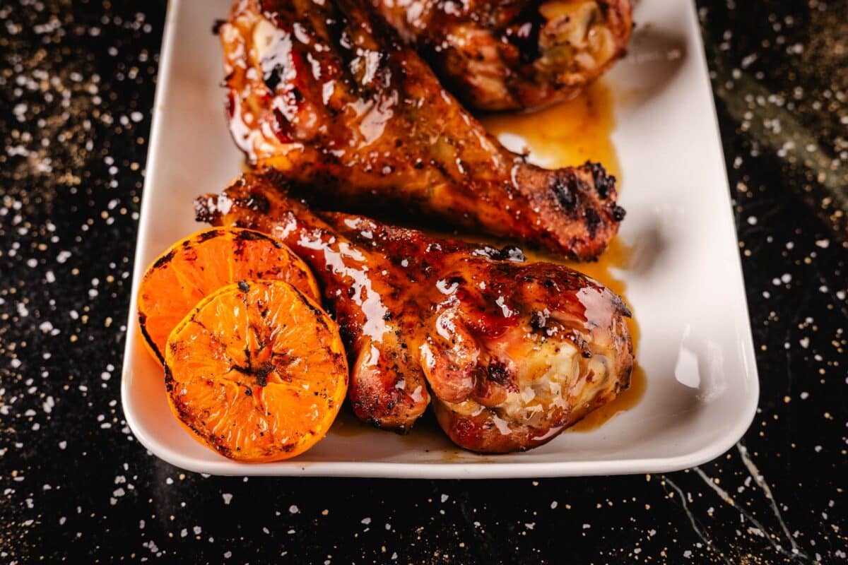 Glazed poultry legs on white platter with halved oranges.