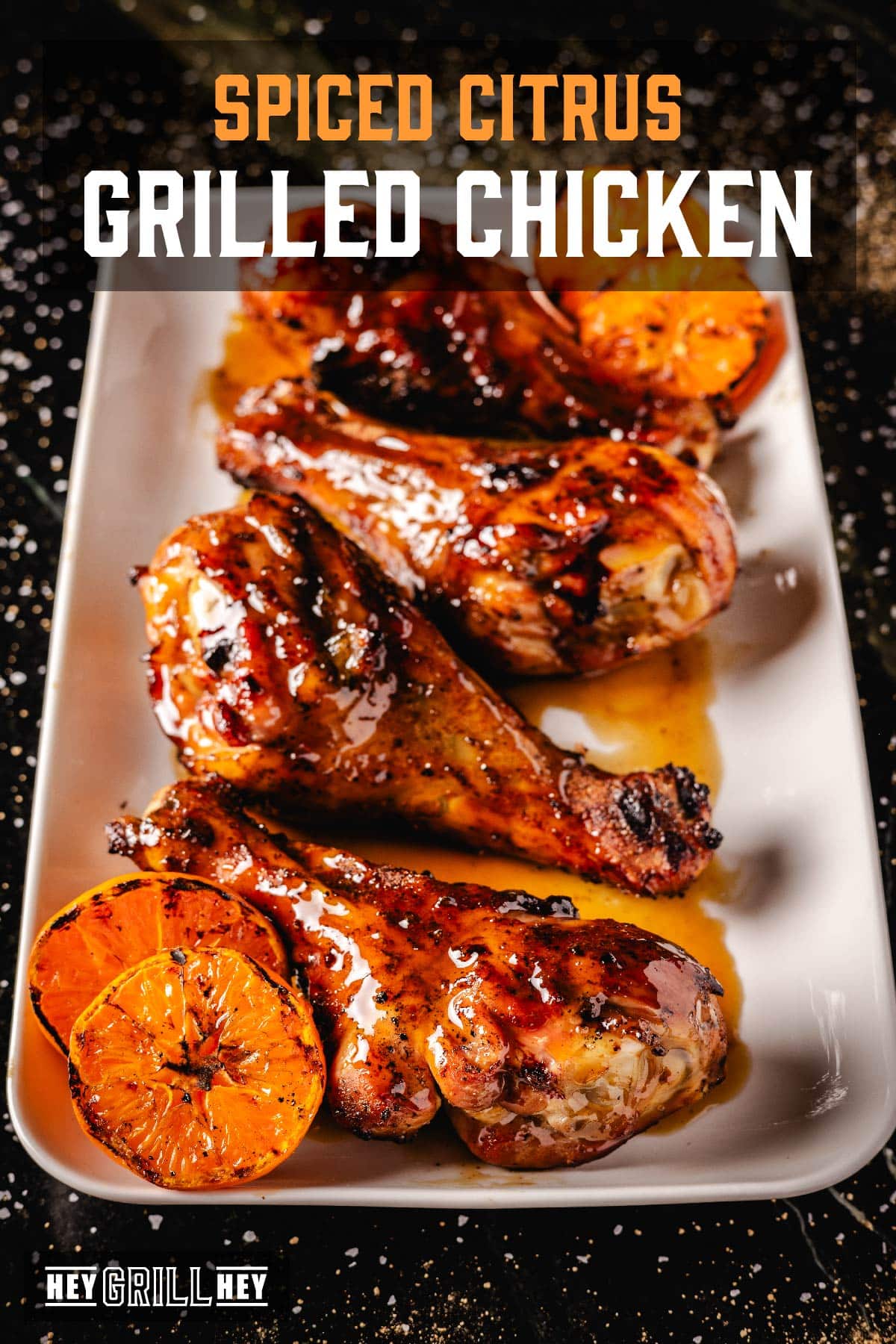 Glazed chicken legs on white platter with orange halves. Text reads "Spiced Citrus Grilled Chicken."