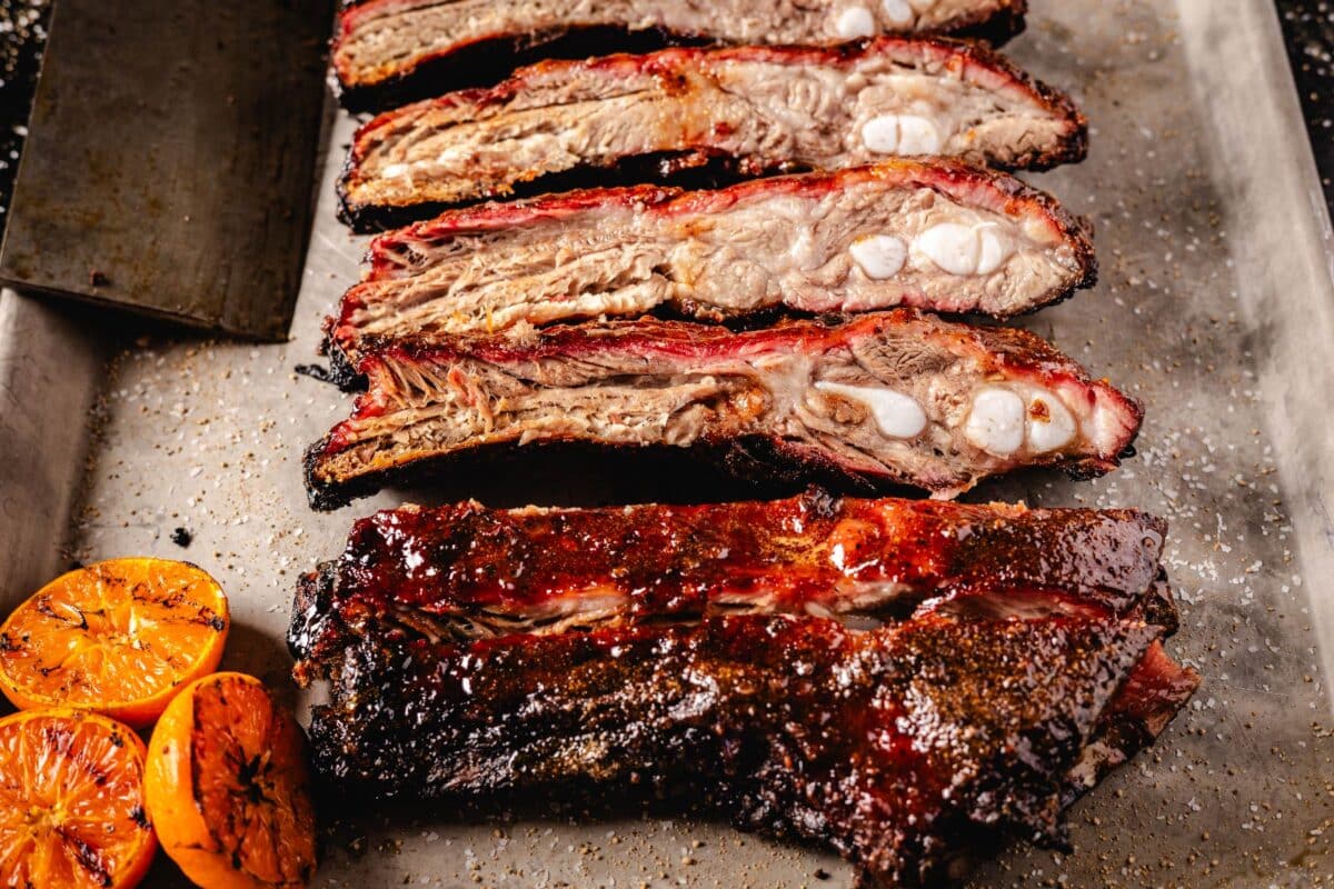 Sliced, smoked ribs on baking sheet with halved oranges.