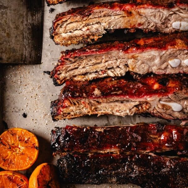 Sliced spare ribs on serving platter next to smoked citrus halves.