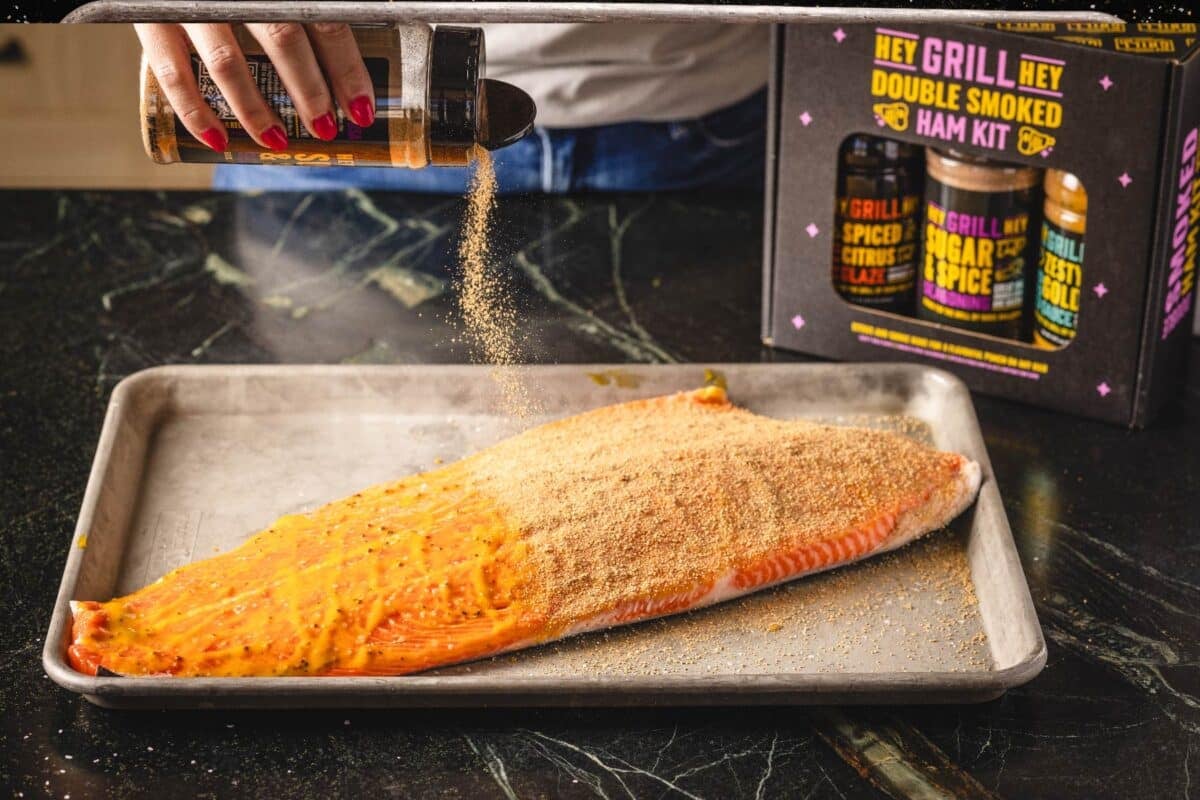 Salmon filet on baking sheet being sprinkled with seasoning.