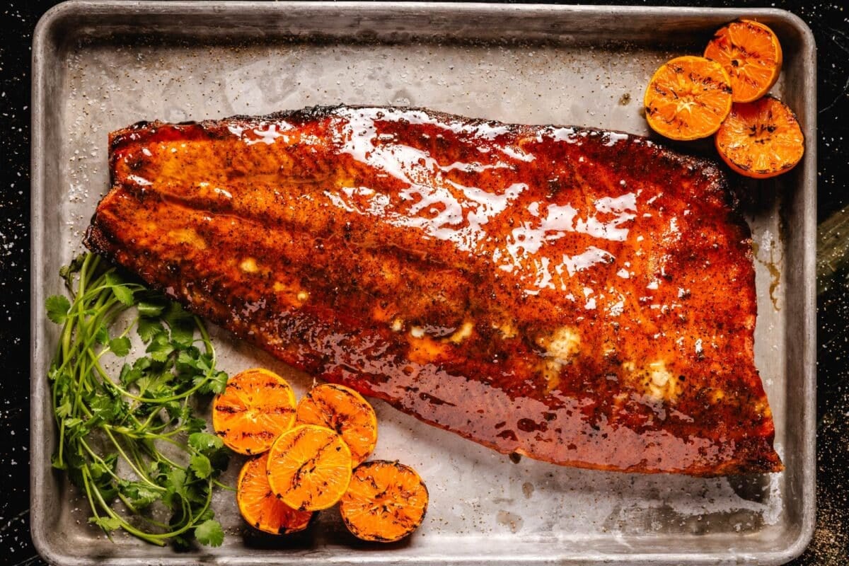 Smoked salmon on baking sheet with citrus slices and herbs.