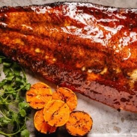 Glazed salmon filet next to grilled orange slices and cilantro leaves.