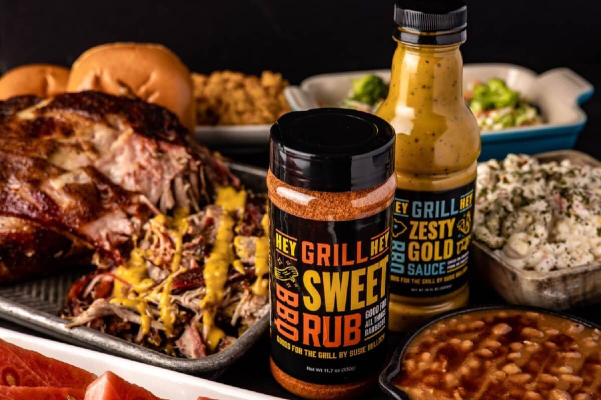 Bottles of Sweet Rub and Zesty Gold BBQ Sauce next to various dishes made with the products.