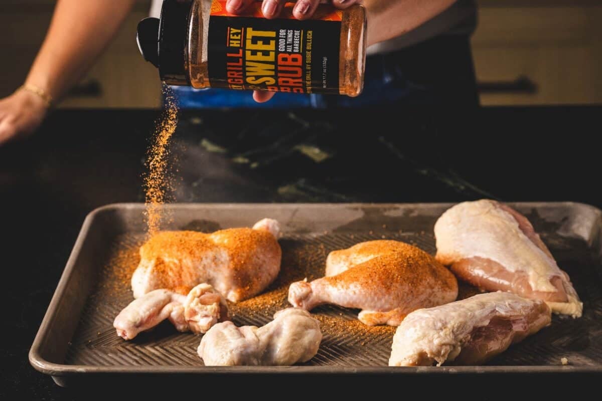 Raw chicken cuts on baking sheet being sprinkled with Sweet Rub.