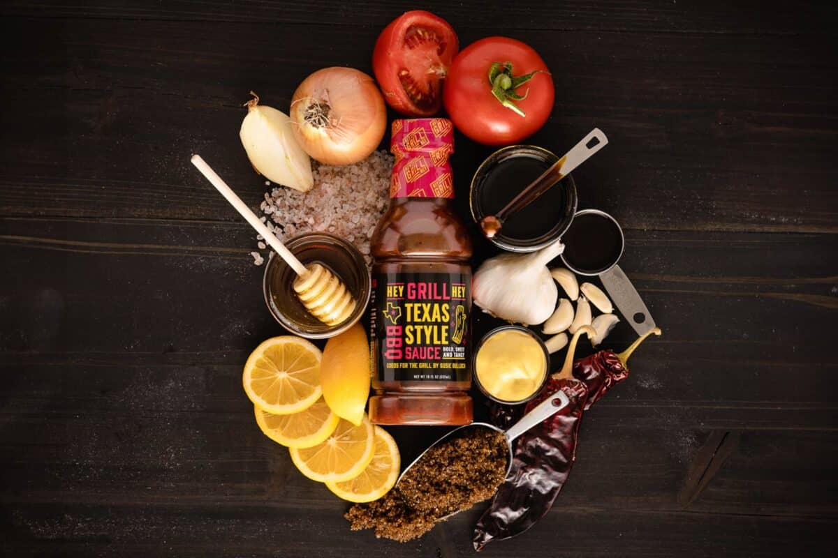 Bottle of Texas Style BBQ Sauce on counter surrounded by raw ingredients.