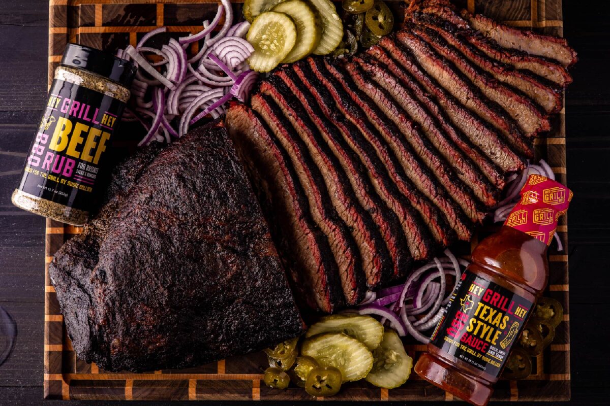 Sliced brisket on wooden platter with sides, and jars of both rub and sauce.