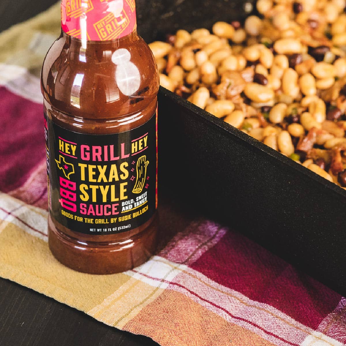 Texas Style BBQ Sauce next to tray of baked beans on table.
