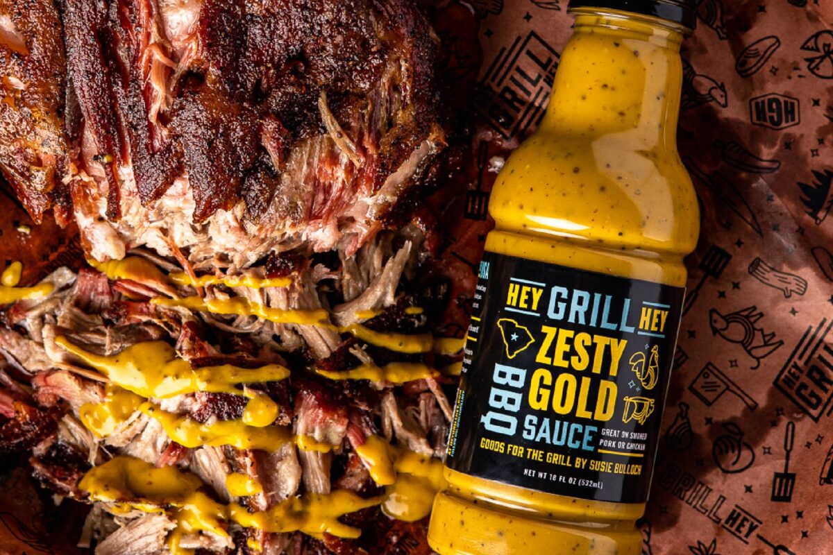 Bottle of sauce next to pulled pork drizzled with mustard.