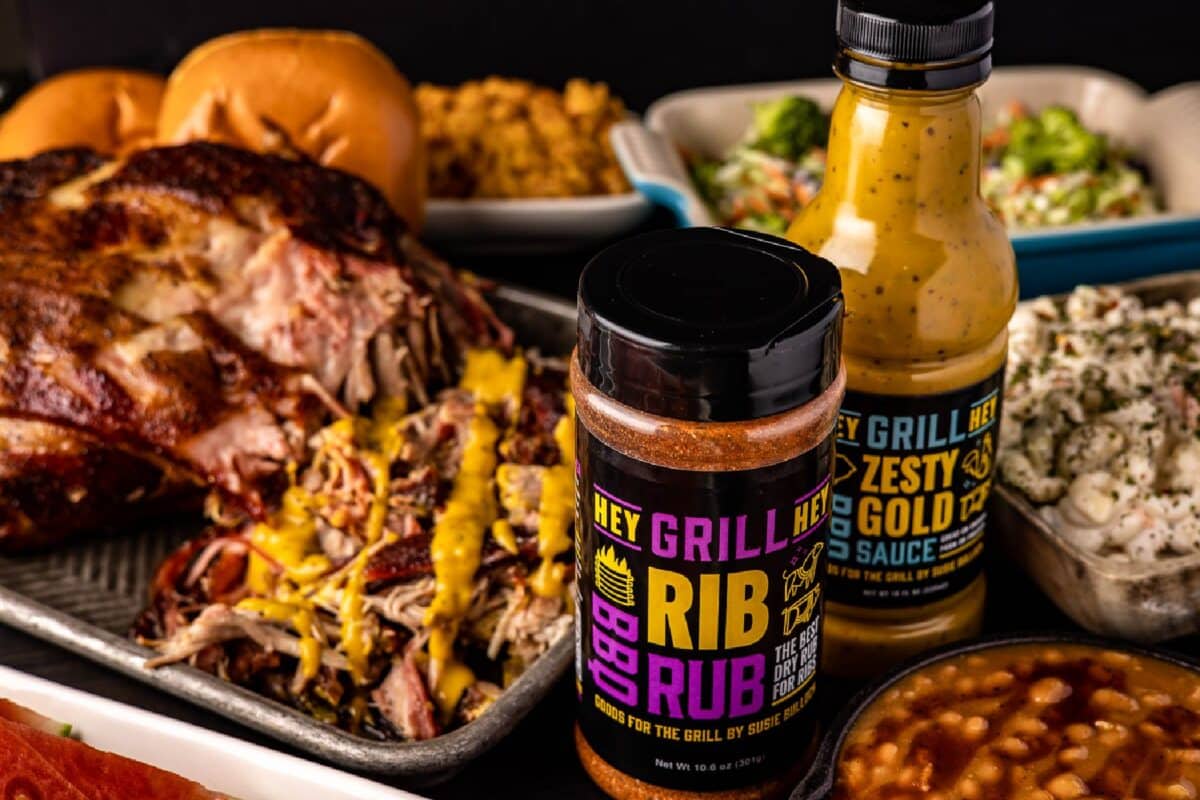 Bottles of Rib Rub and Zesty Gold BBQ Saue next to platter of pulled pork.