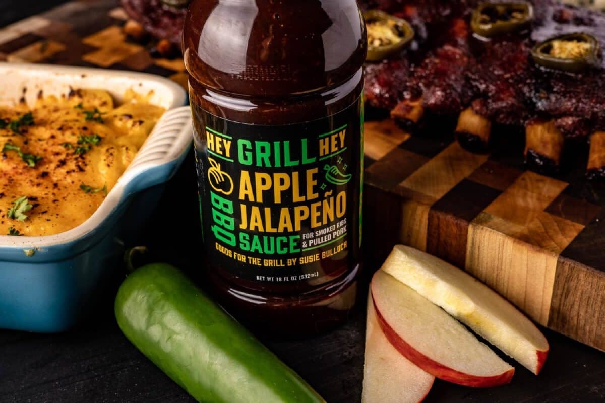 Bottle of Apple Jalapeño Sauce on cutting board next to a dish of potatoes.