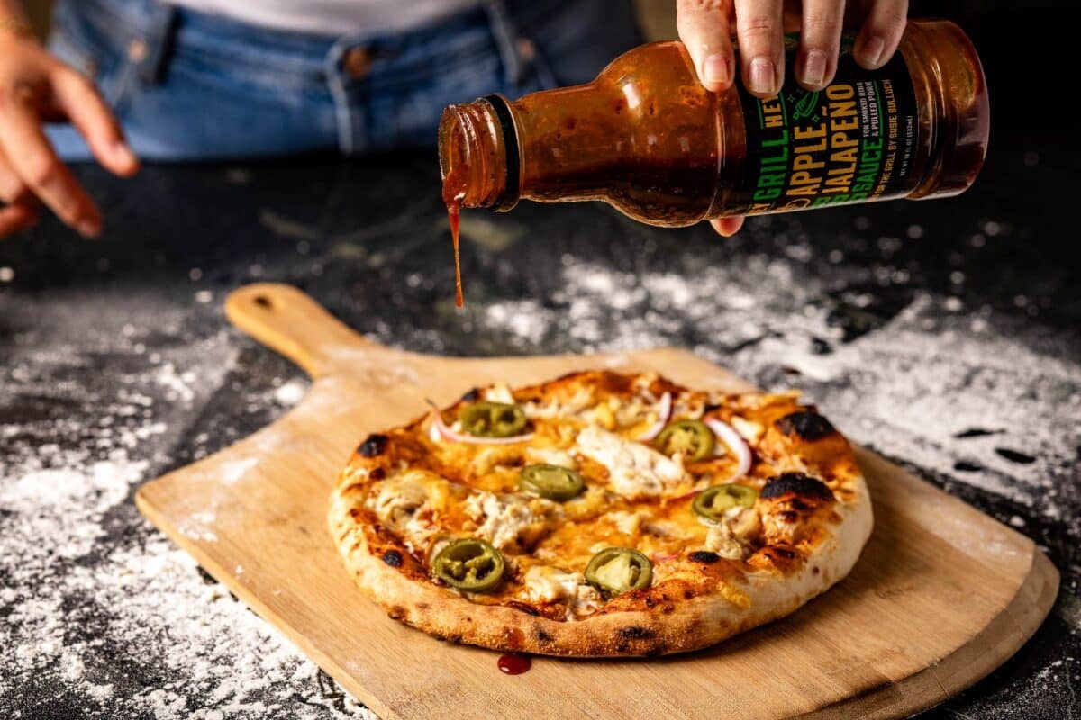 Chicken pizza on a wooden peel being drizzled with BBQ sauce.