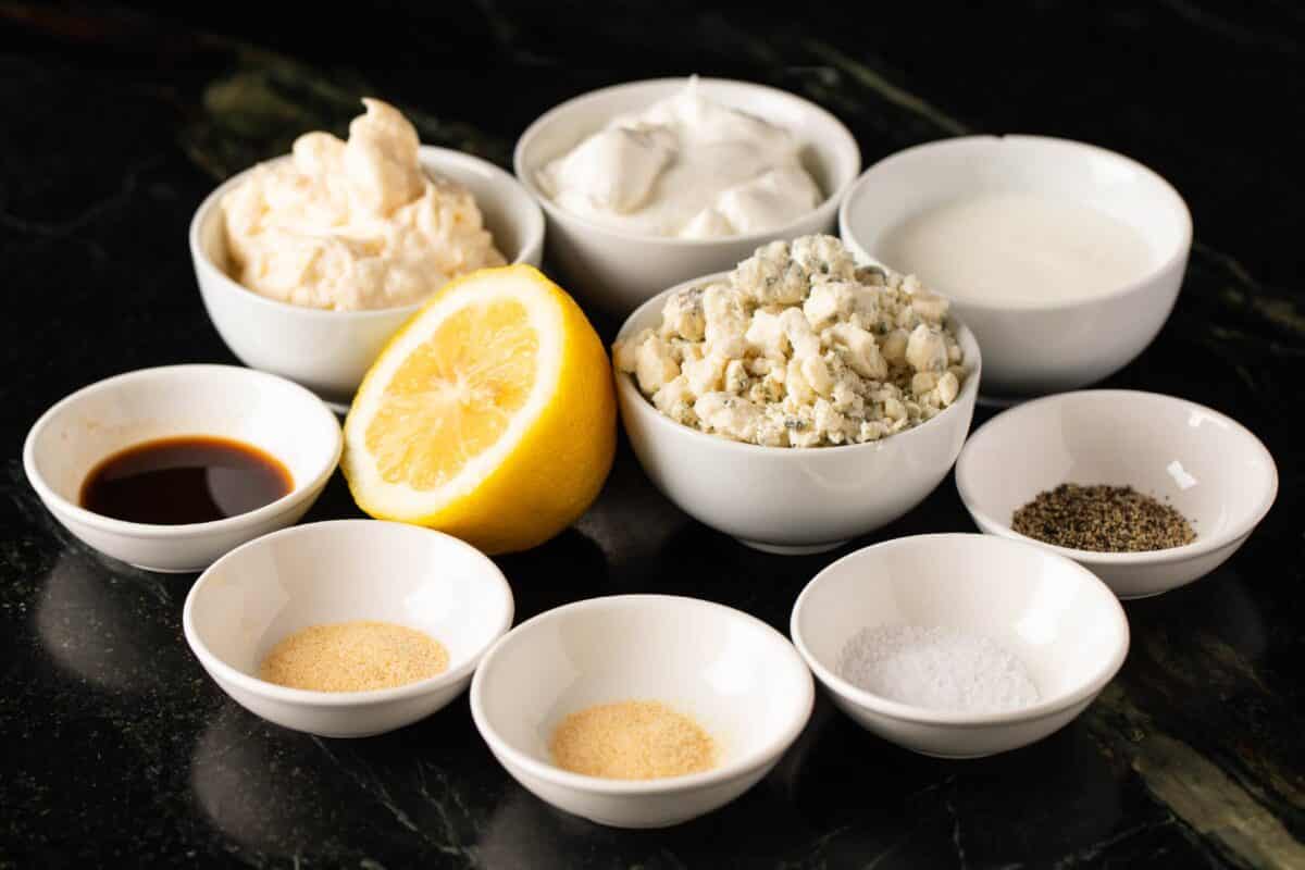 Lemon halve and white bowls of raw ingredients on countertop.