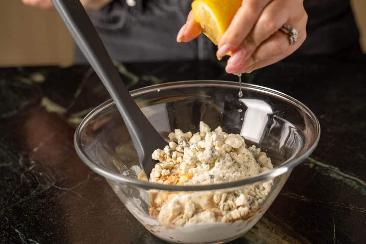 Juice being squeezed from lemon into glass bowl of ingredients.