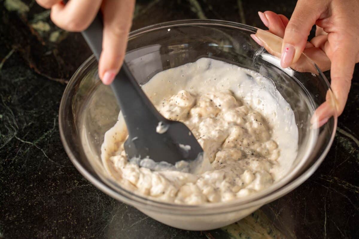 Rubber spatula mixing blue cheese dressing in glass bowl.