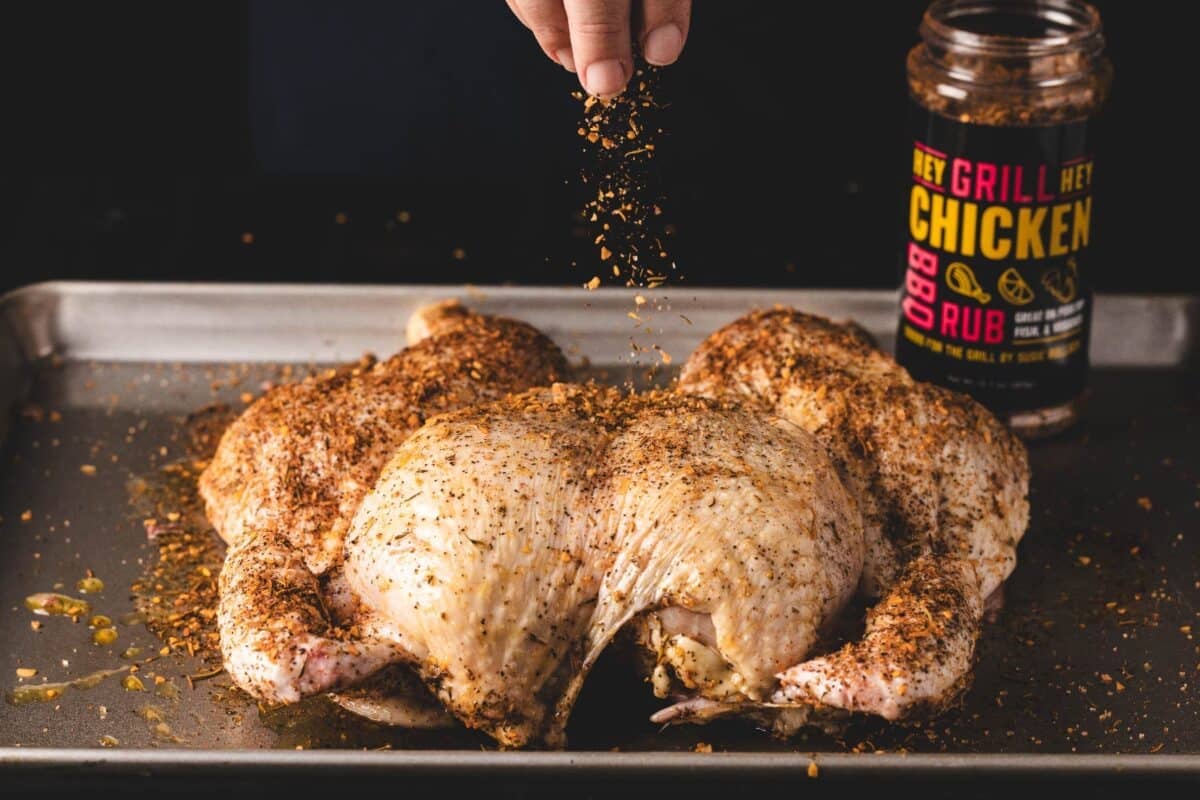 Spatchcocked turkey on a baking sheet being sprinkled with seasoning.