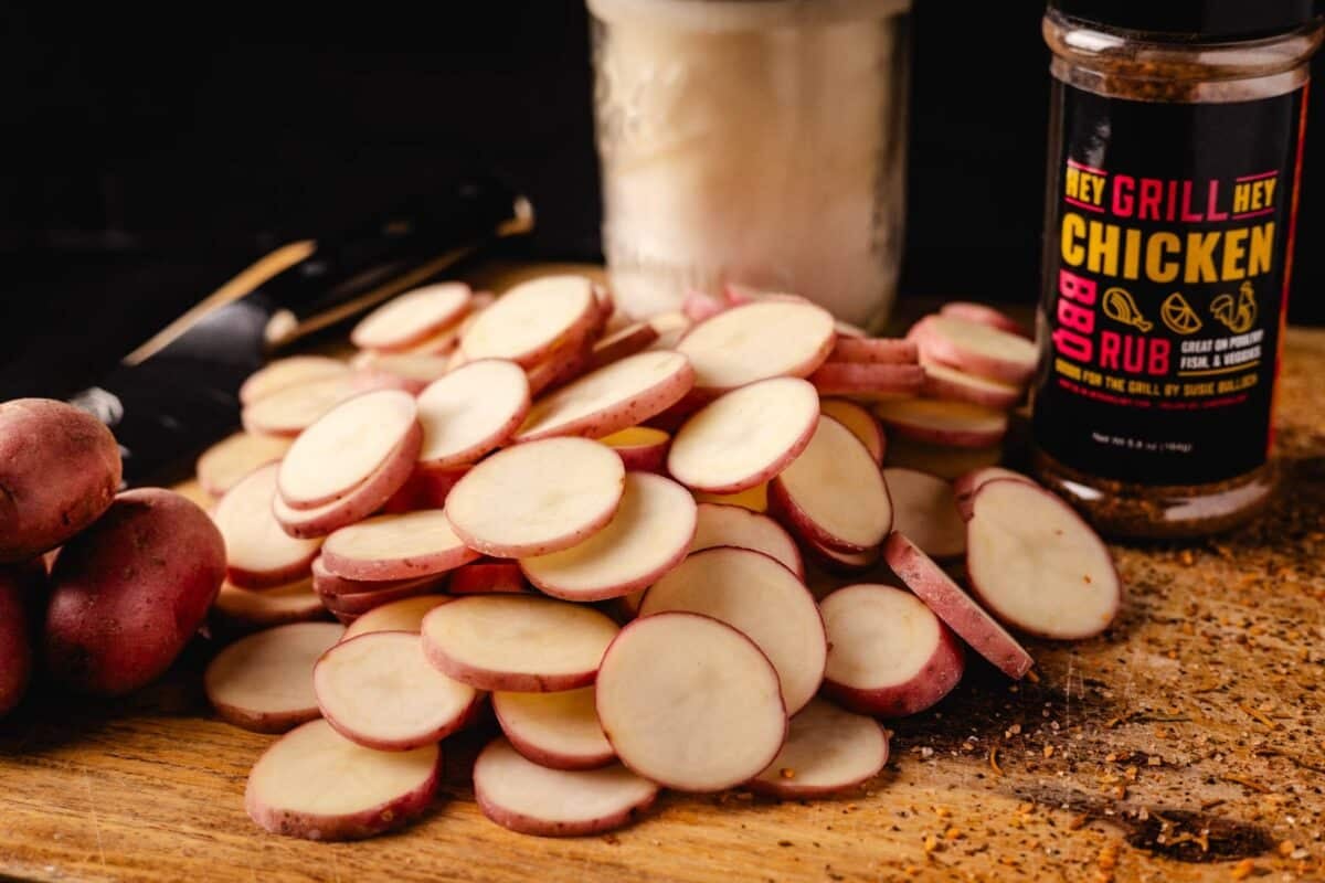 Sliced potatoes on a cutting board in front of a bottle of seasoning.