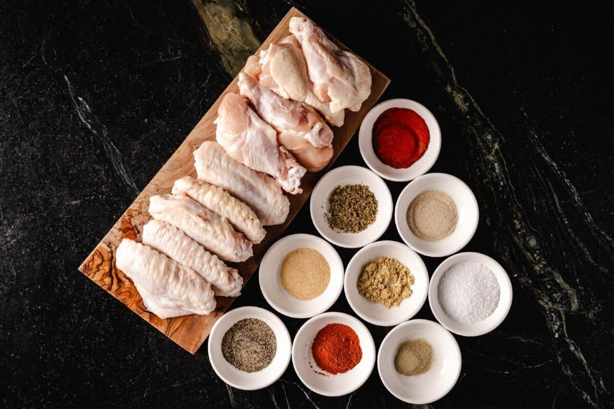 Raw chicken wings, and ingredients for dry rub in white bowls, on wooden cutting board.