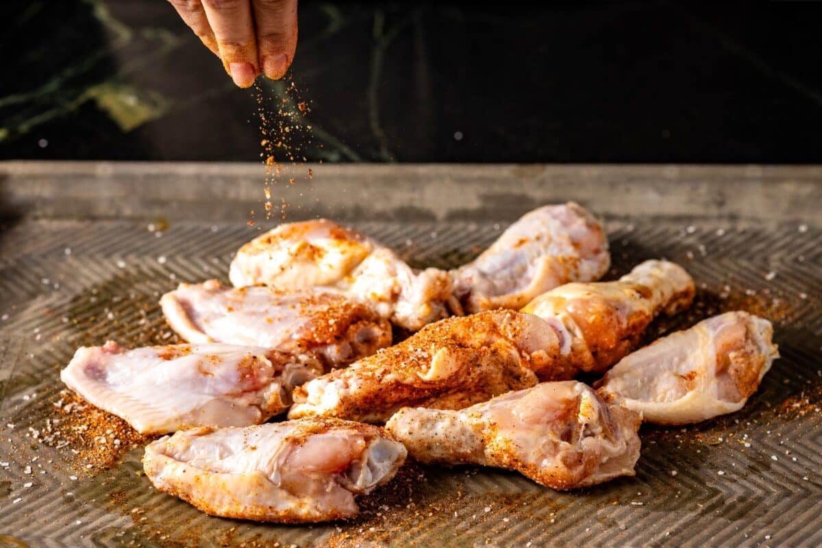 Cajun seasoning being sprinkled onto chicken wings on baking sheet.