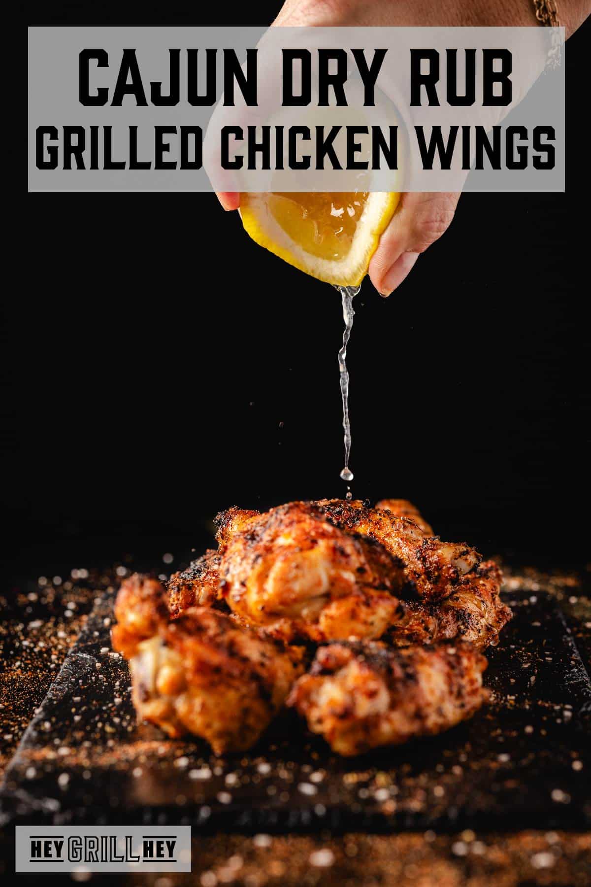 Lemon juice being squeezed from lemon onto pile of wings on platter. Text reads "Cajun Dry Rub Grilled Chicken Wings."