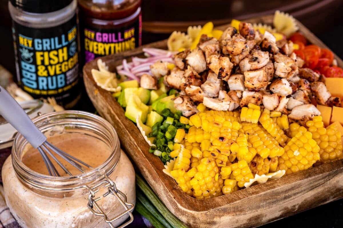 Mason jar of homemade BBQ ranch sauce next to tray of salad ingredients, in front of sauce and rub jars.